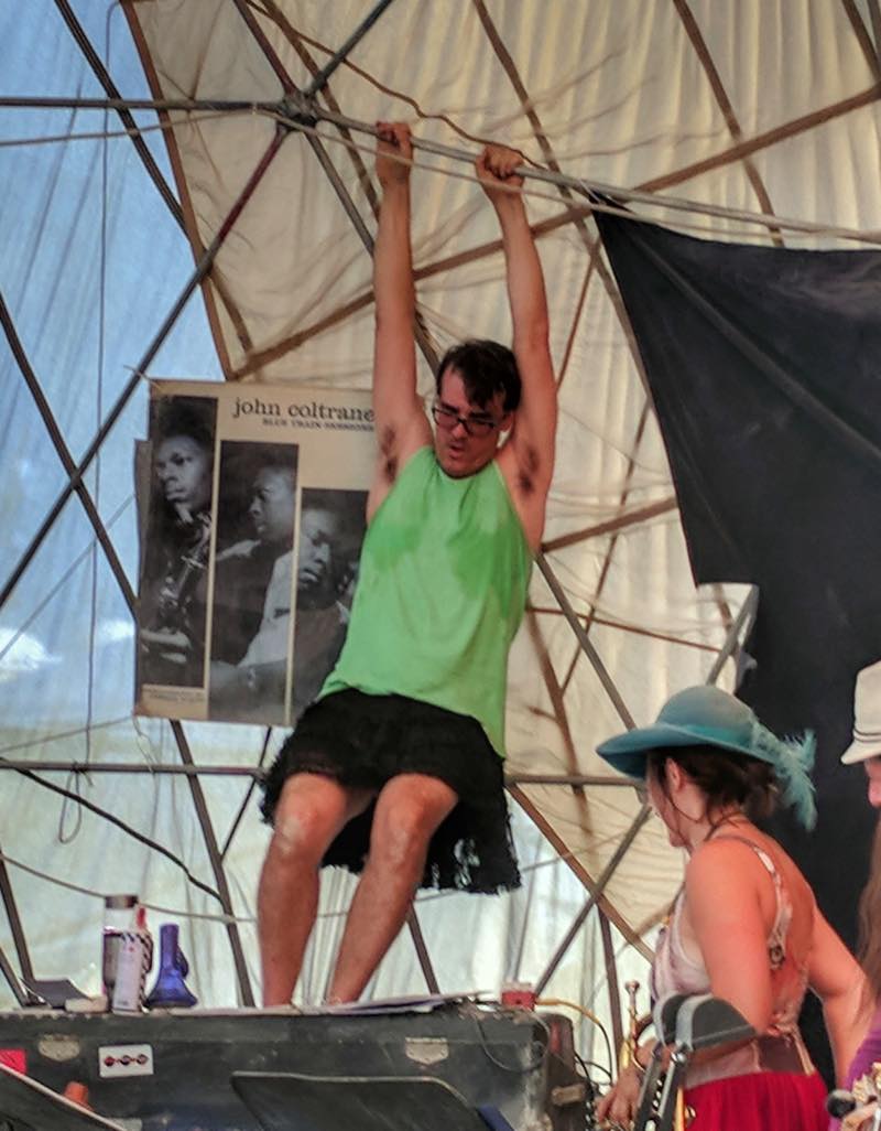 A dancer hangs by both hands from the dome frame above the stage, beside a John Coltrane Blue Train poster.