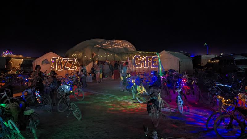 The camp at night, the words JAZZ and CAFE in warm bulb lettering either side of the entrance, dozens of lit bicycles parked in front.