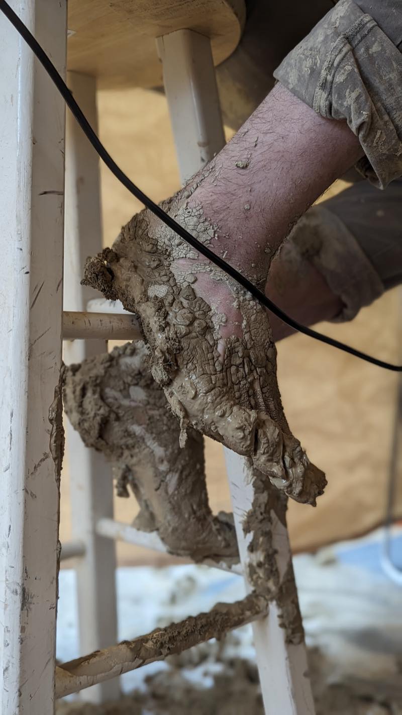 A bare foot propped on a chair rung, playa mud caked over it and dried into thick cracked plates.