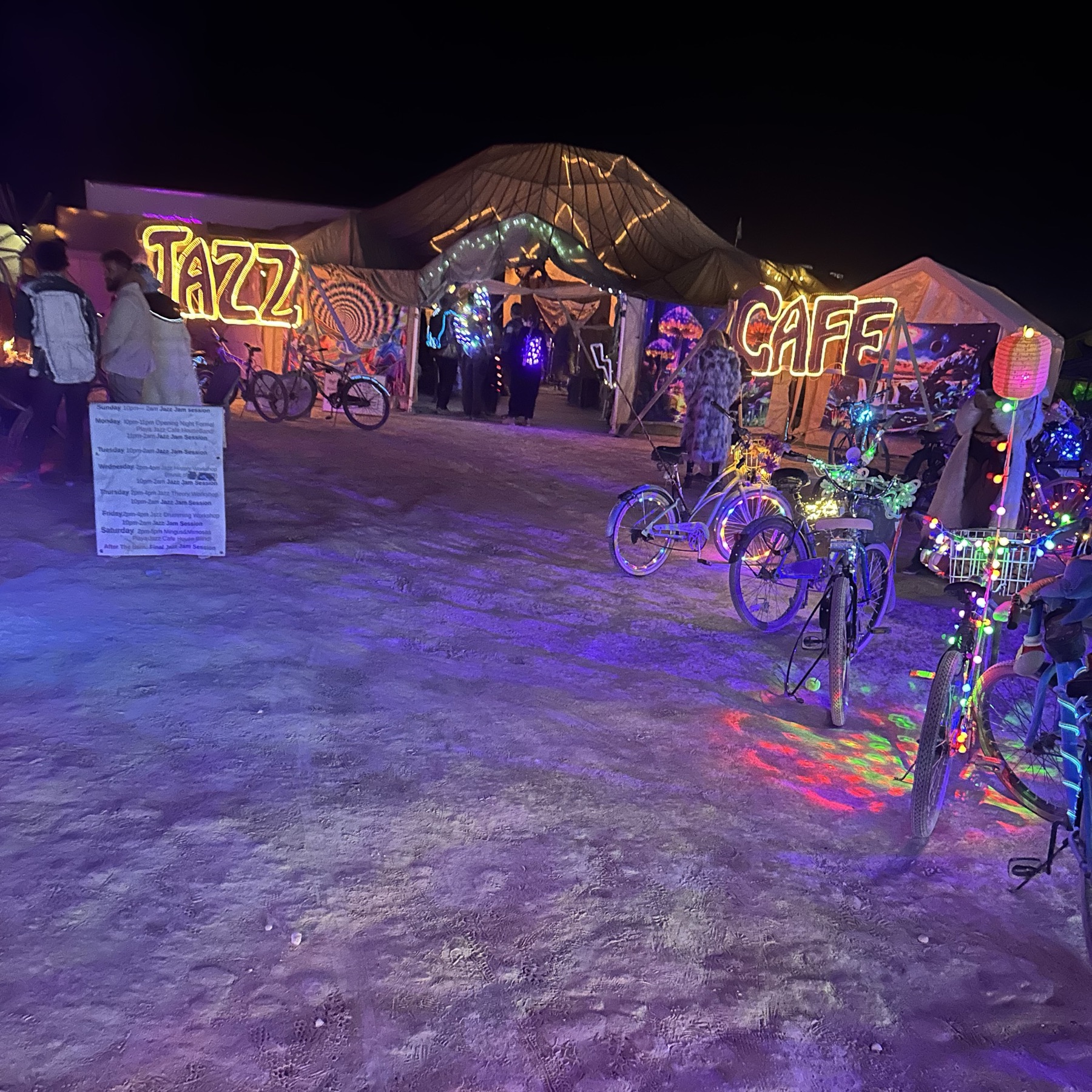The Playa Jazz Caf&eacute; frontage at night in Black Rock City, lit in amber and violet.
